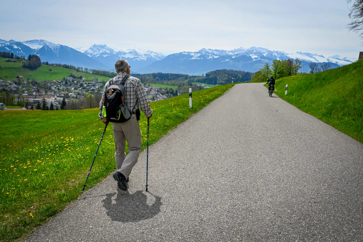 Ein Mann mit Wanderstöcken läuft auf einer Strasse.